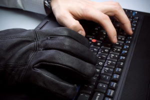 Hands typing, one wearing a black glove to imply cyber crimes against data privacy