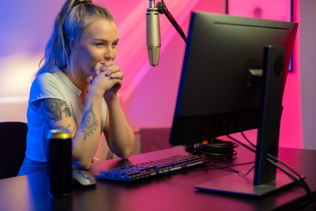 Tattooed gamer girl sitting at a PC smiling.