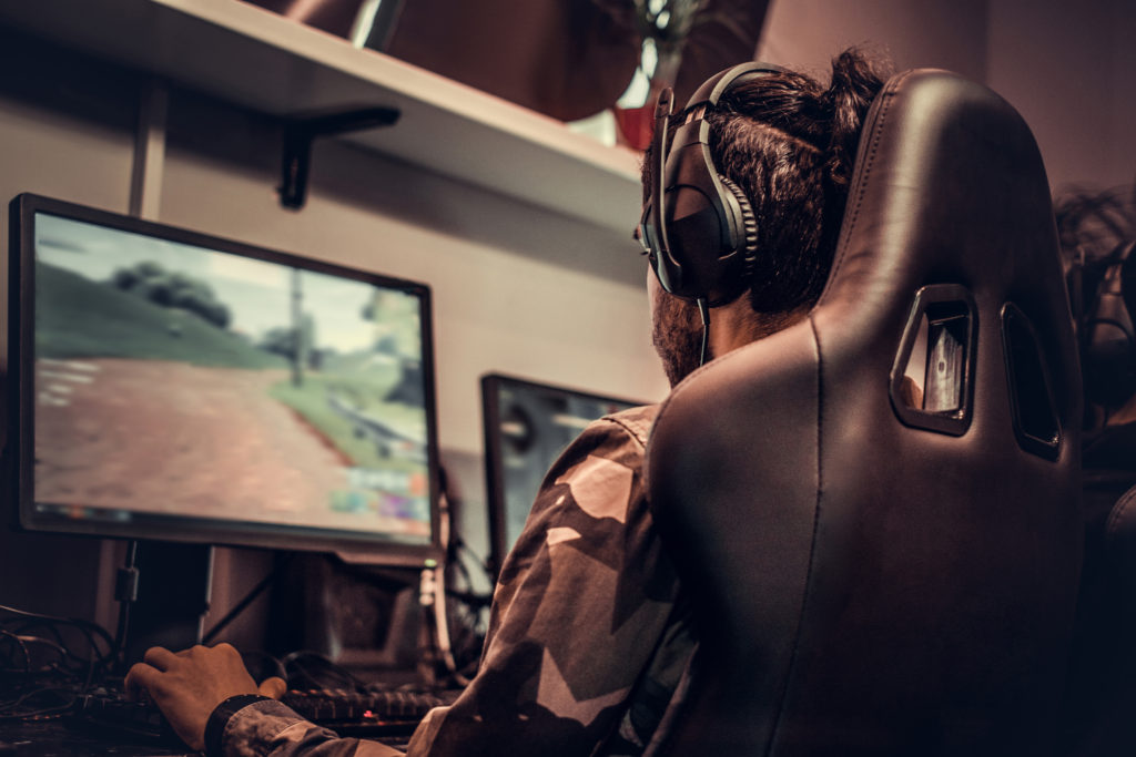 Male presenting gamer wearing a headset and sitting at a PC.